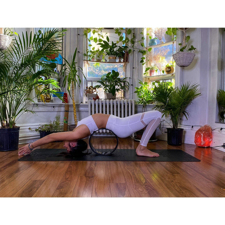 ANJANEASANA ( LUNGE) using a yoga wheel with lotus flower laser engraving and 7 chakras on the inner circle, inside oblong house studio